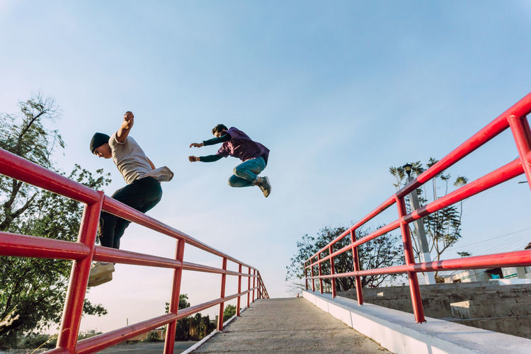 Low angle view of men jumping on footbridge against sky