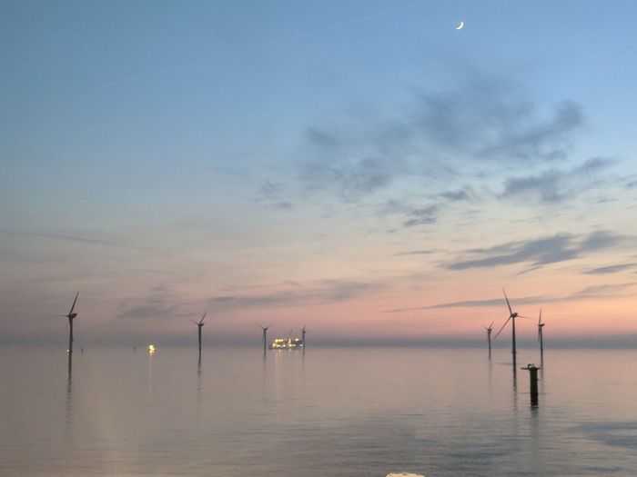 Scenic view of sea against sky during sunset with wind turbine