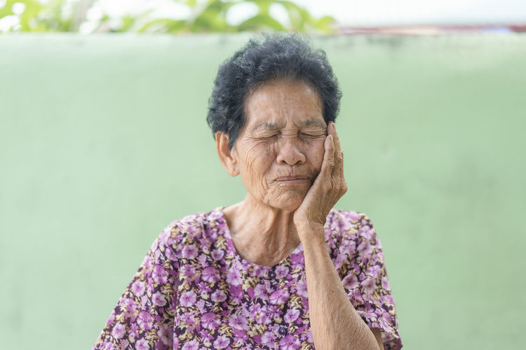 Senior black-haired woman touching the mouth with hand with painful expression because of toothache 