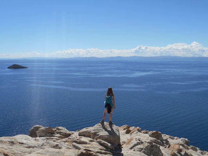 Rear view of female hiker with backpack standing on rock against sea