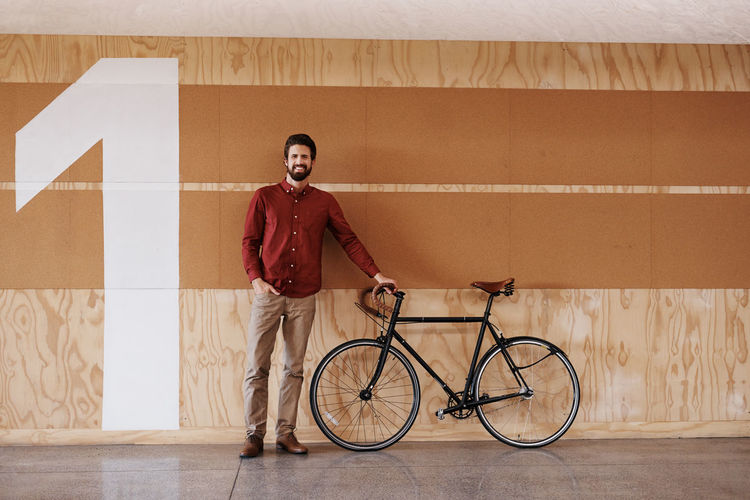 Portrait of young man bicycle against wall