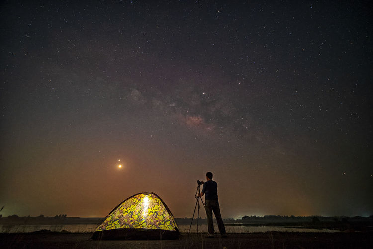 Rear view of silhouette man with camera standing against sky at night