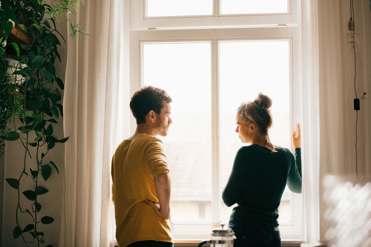 Young couple standing against window at home