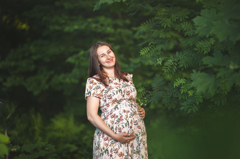 Portrait of pregnant woman standing against trees in forest