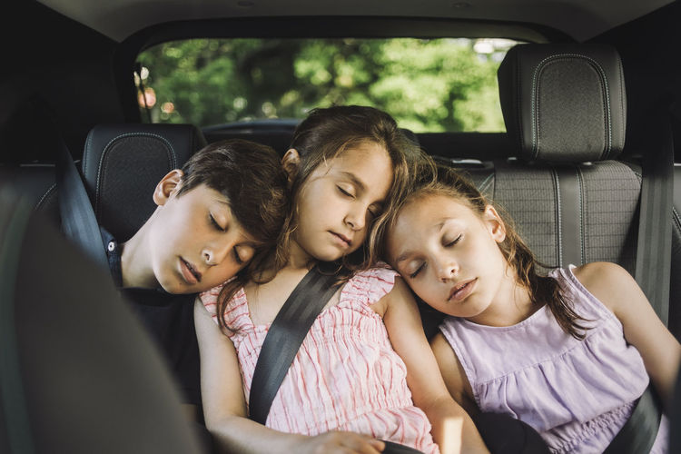 Tired siblings sleeping on back seat while traveling in car
