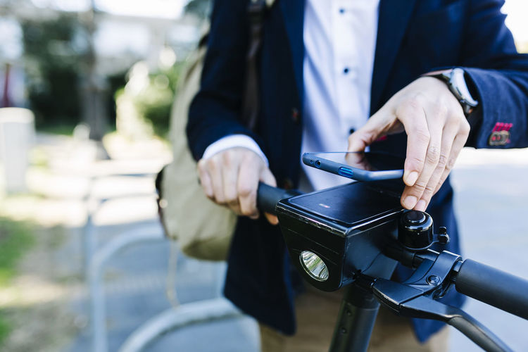 Businessman renting bicycle through mobile phone while standing at bicycle station