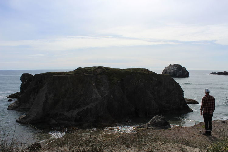 Rear view of man standing on cliff by sea against sky