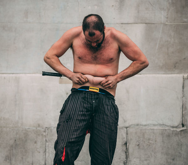Shirtless man performing while standing against wall