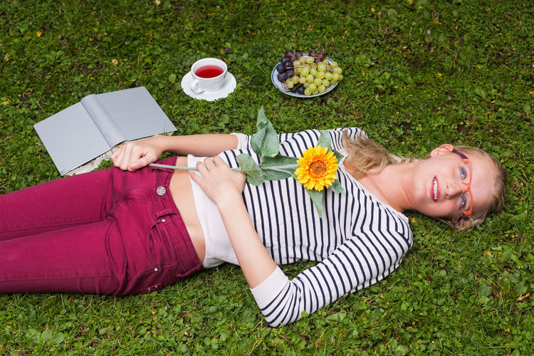 High angle view of young woman holding flower while lying on grassy field