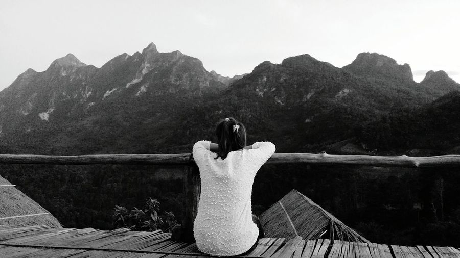 Rear view of woman leaning on bamboo railing while sitting against mountains