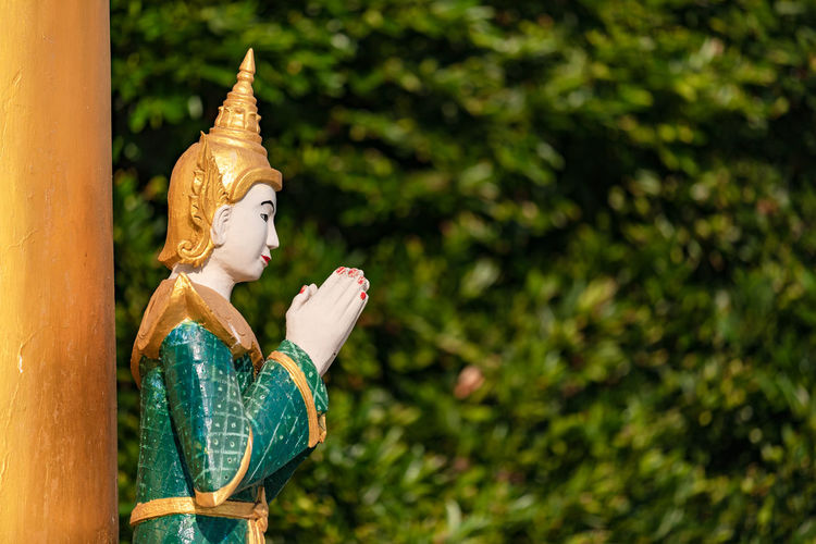 A praying buddha statue with folded hands in a temple against a natural background in myanmar