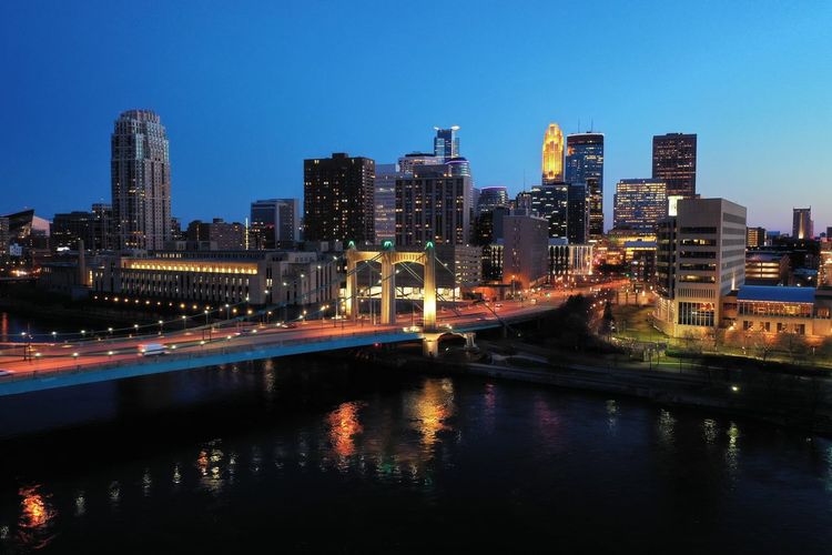 Illuminated buildings by river against clear sky at night