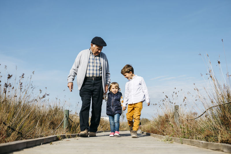 Grandfather strolling with his grandchildren hand in hand on boardwalk