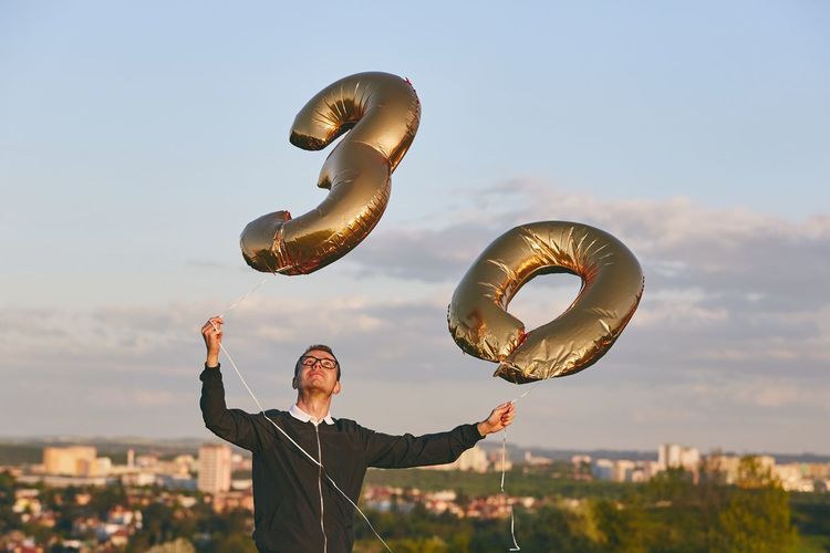Man holding number 30 helium balloons against cityscape