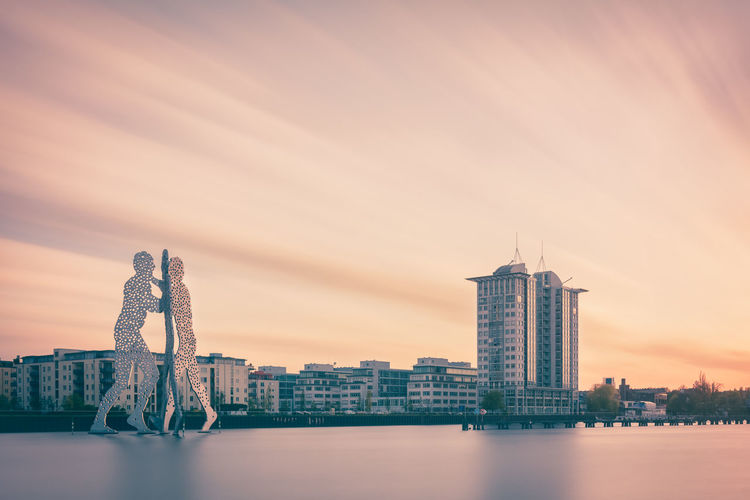 Molecule man over spree river against sky during sunset