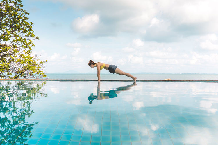 Woman exercising against sea at infinity pool