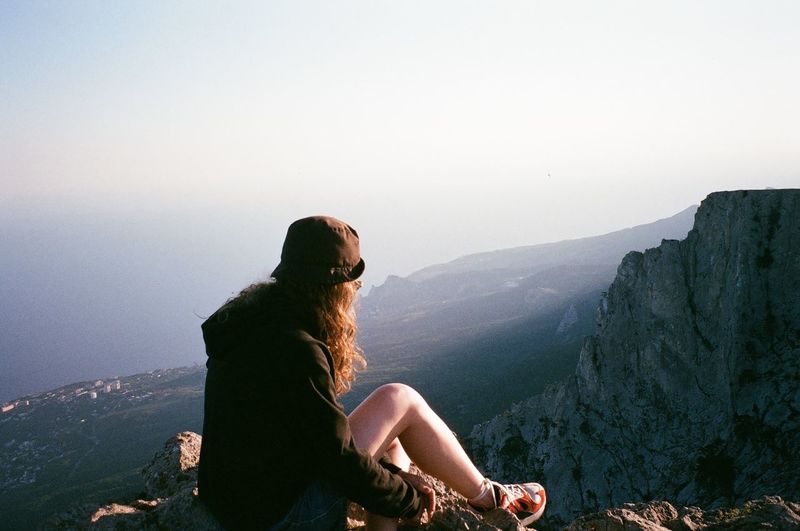 Young woman sitting by cliff looking at mountain