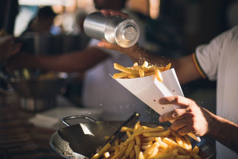 Midsection of man dusting salt on french fries
