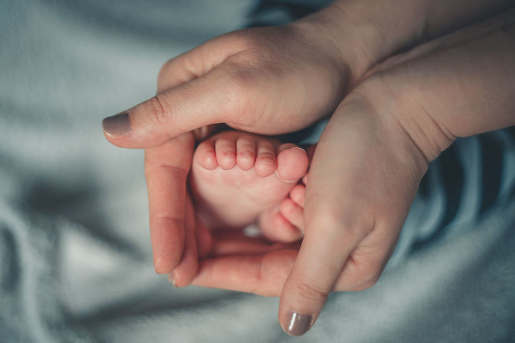 Cropped hands of woman holding baby boy feet on bed