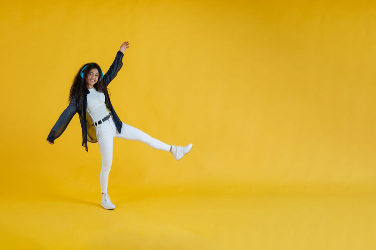Full length of woman jumping against yellow wall