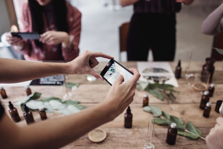 Cropped hand of woman photographing perfume bottles on table at workshop
