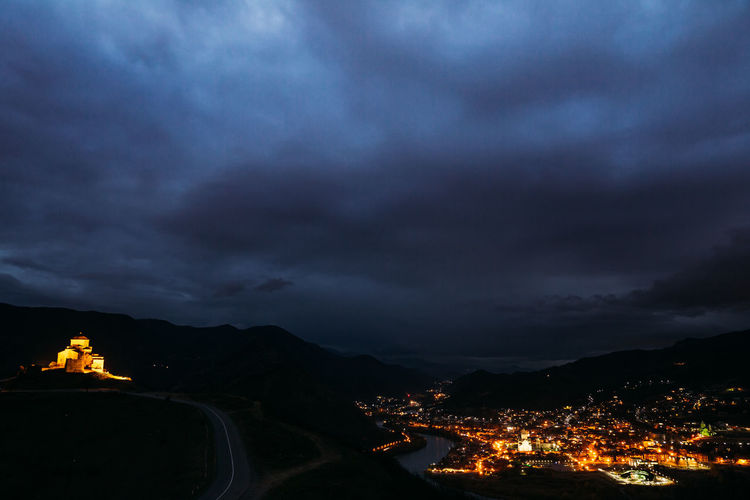 Illuminated townscape against cloudy sky at night