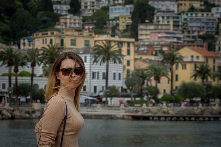 Portrait of woman wearing sunglasses standing against buildings
