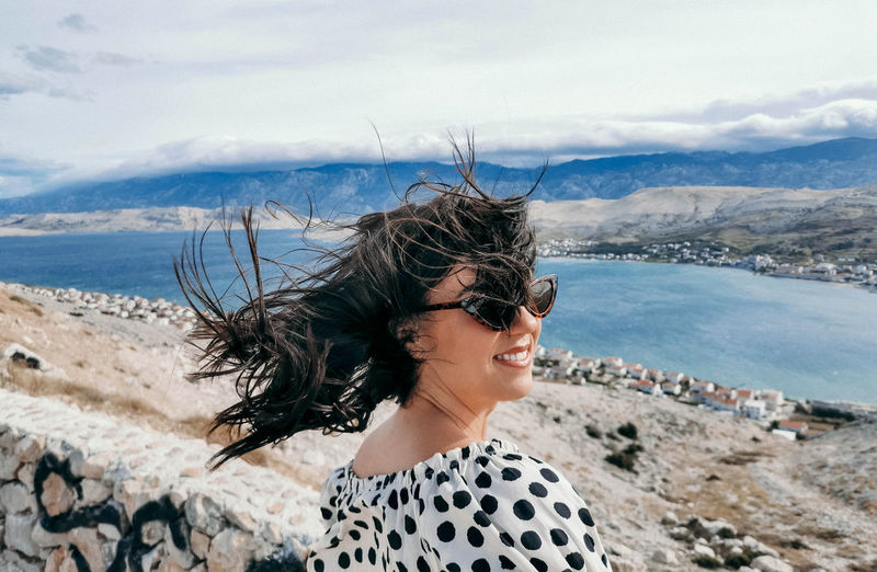 Rear view of young woman on viewpoint over sea. wind blowing hair.