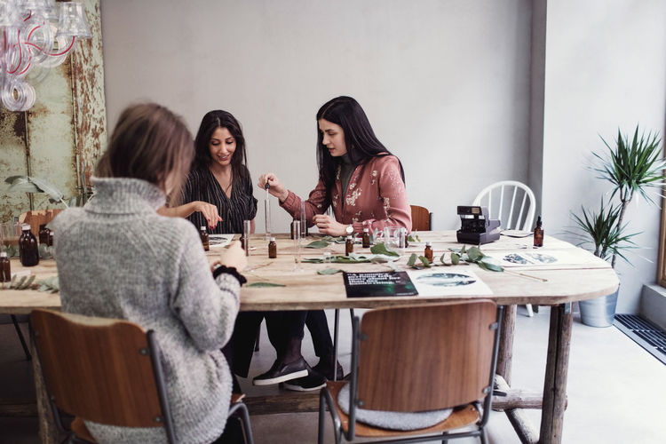 Female colleagues preparing perfume while sitting at table in workshop