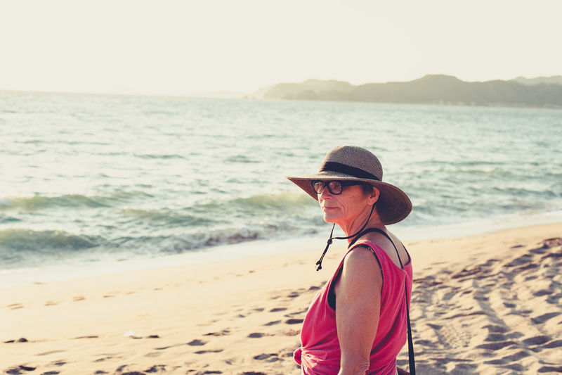 Senior woman in straw hat at the beach at sunset