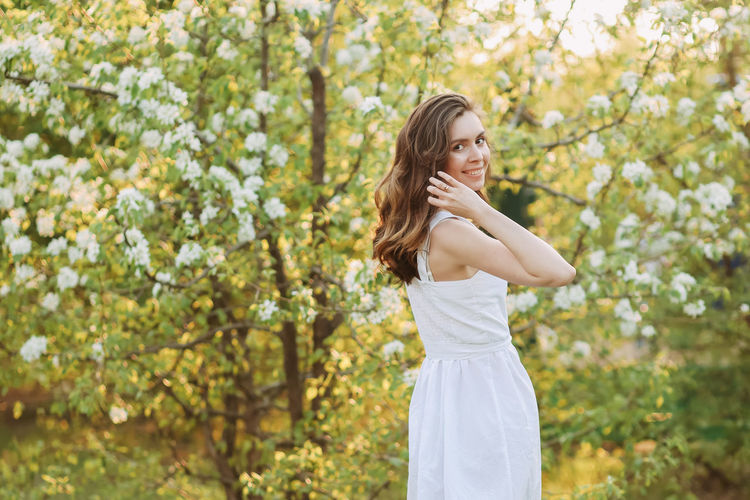 A cute happy young woman with a hairstyle in a white dress is walking enjoying nature in the summer