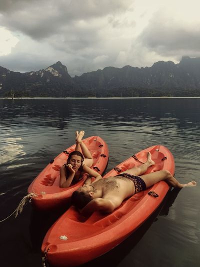 Full length of couple lying on canoes in lake against sky