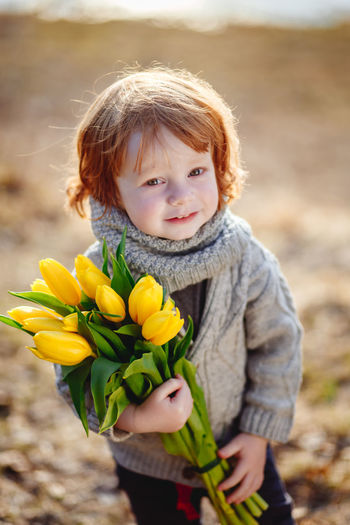 Portrait of cute boy holding yellow flowers on field