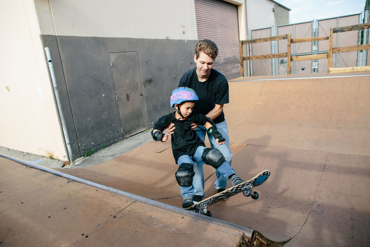 Skateboarding instructor holds boy helping him turn on half pipe