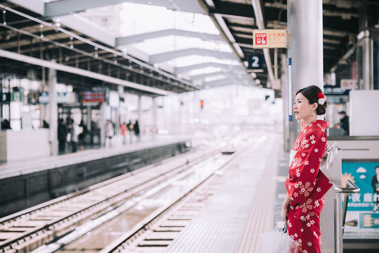 Side view of woman with umbrella standing at railroad station