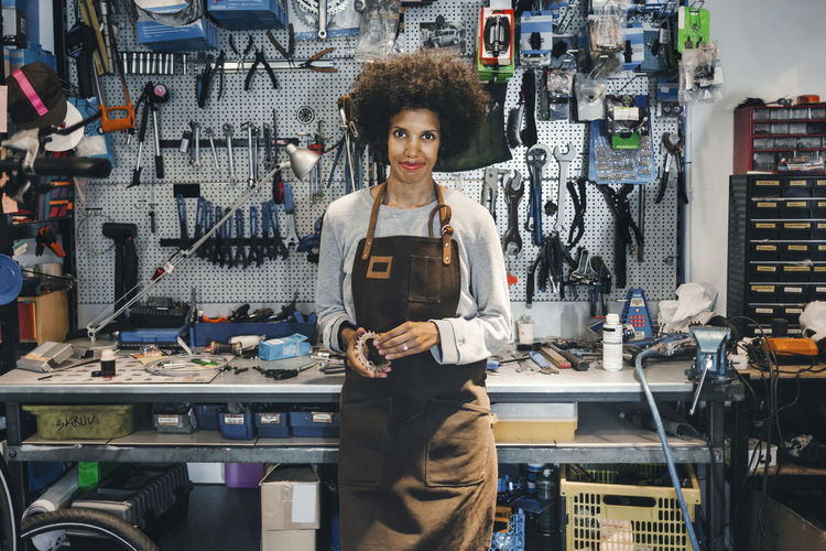 Portrait of confident female mechanic holding bicycle gear in workshop