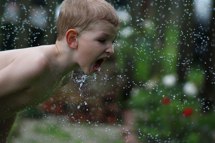 Close-up of shirtless boy playing with water in yard