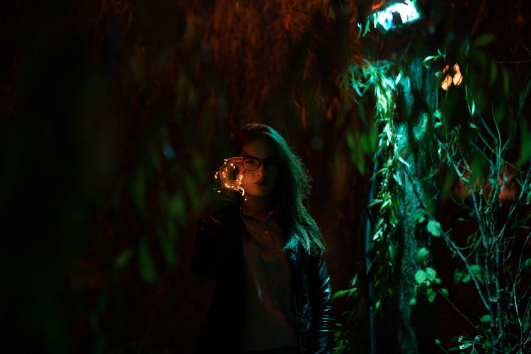 Portrait of young woman holding illuminated string lights at night