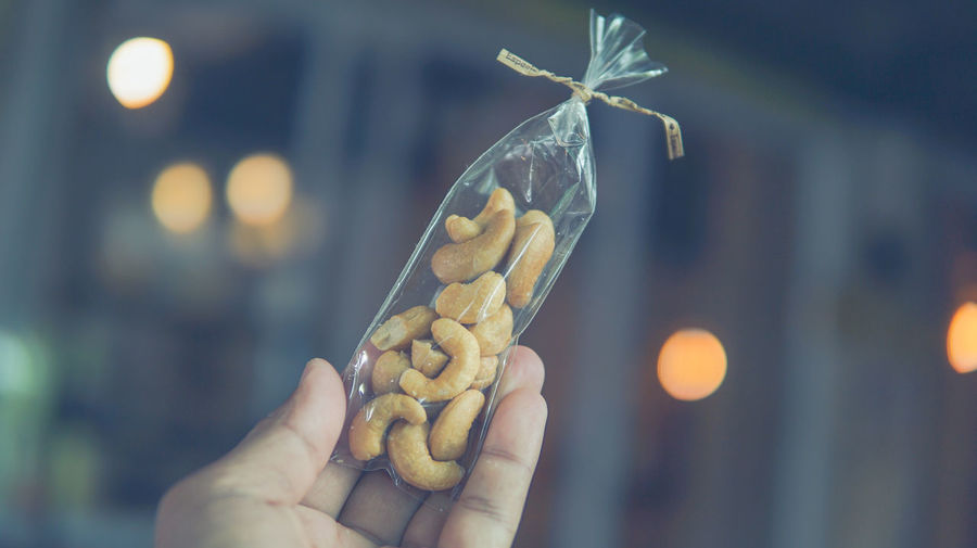 Cropped hand of person holding cashew in plastic