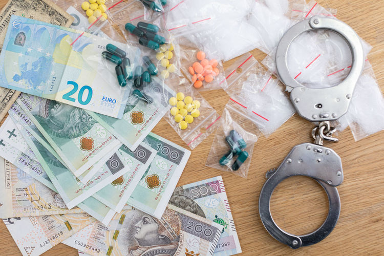 On the table lies currency in banknotes of different countries and drugs in pills and handcuffs.