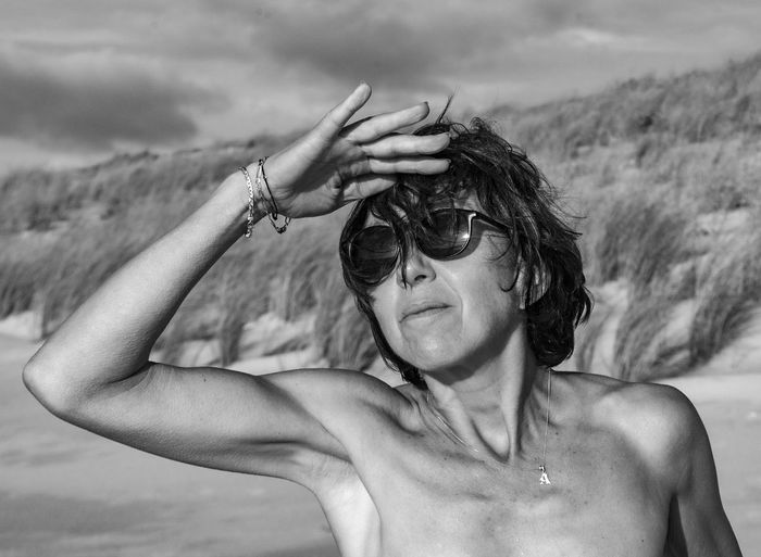 Shirtless woman wearing sunglasses shielding eyes at beach