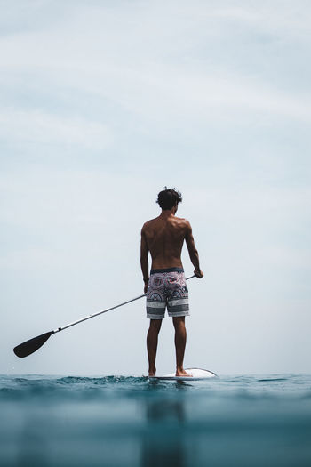Rear view of man paddleboarding in sea against sky