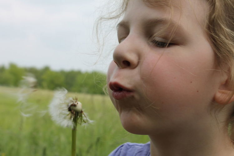 Close-up of girl with dandelion flower on field