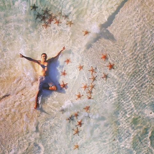 High angle view of shirtless man with arms outstretched lying in sea