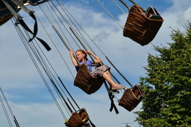 Low angle view of girl on chain swing ride against sky