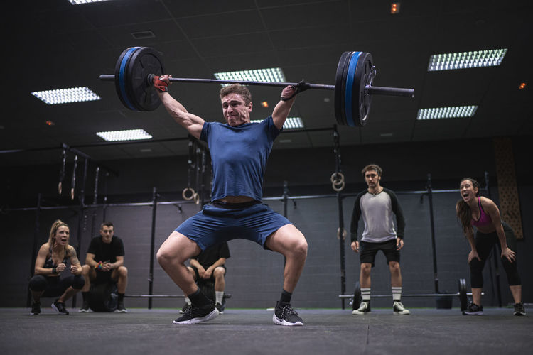 Athletes cheering man picking barbell while standing at gym