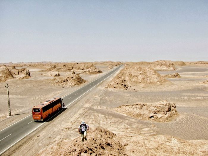 People walking on road in desert against clear sky