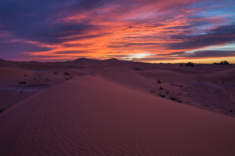 Scenic view of desert against cloudy sky during sunset
