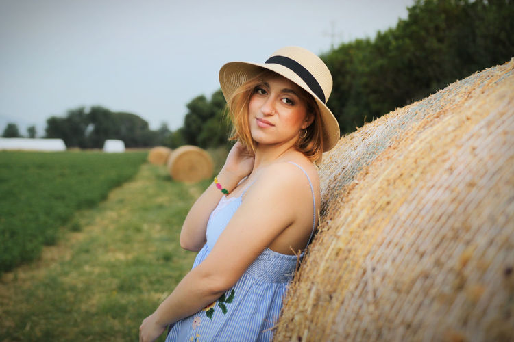 Portrait of young woman standing by haystack