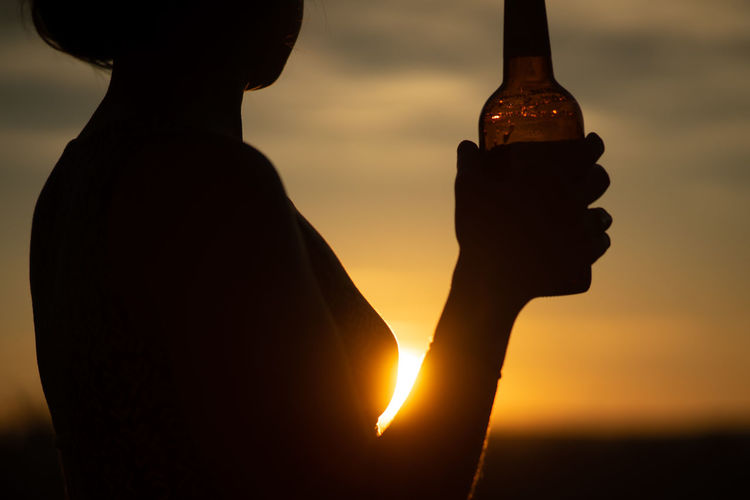 Silhouette man holding bottle against sky during sunset